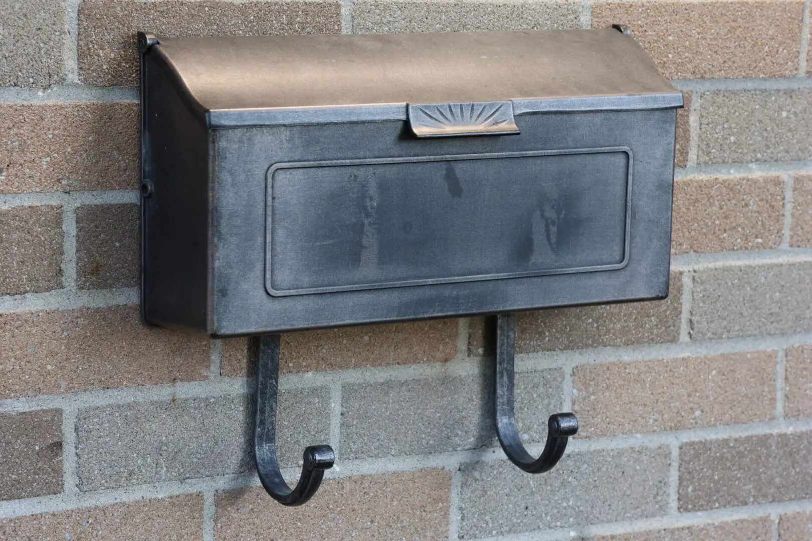 Traditional black metallic mailbox mounted on a brick wall with hooks.